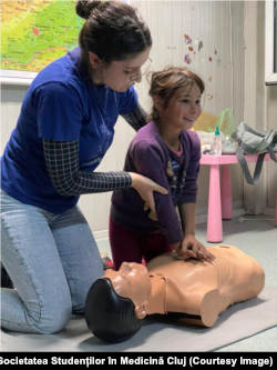 O studentă voluntar de la „Micii sanitari” (de la Societatea Studenților în Medicină Cluj) îi explică unui copil din Pata Rât, Cluj, cum să acorde primul ajutor în caz de urgență.