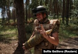 Військовослужбовець 14-ї ОМБР ЗСУ «Князь Роман Великий» несе снаряд для 155-мм самохідної гаубиці М109 поблизу Куп'янська, 19 липня 2023 року