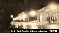 Една от снимките на Емин Емин. На преден план се виждат локви и остатъци от сняг. Била е много студена зима, казват в спомените си оттагава българските турци. На заден план се виждат групи на хора от селото. Двете сгради са на киното и на гастронома.