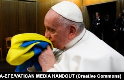 Папа Римський Франциск цілує прапор України зі знищеного армією РФ українського села, який йому подарували разом і браслетом із металу з «Азовсталі» та пачкою солі з останньої партії комбінату «Артемсіль». Ватикан, 24 лютого 2023 року