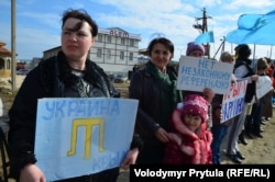Locuitori din peninsulă, purtând pancarte și steaguri cu simboluri ale tătarilor din Crimeea, la o acțiune de protest față de organizarea „referendumului” în peninsulă, 14 martie 2014