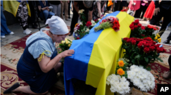 A woman kneels at the coffin of activist and soldier Roman Ratushniy during his memorial service in Kyiv on June 18, 2022.
