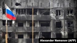 Російський прапор на тлі вигорілого – внаслідок бомбардувань і обстрілів російської армії –житлового будинку Маріуполя. 11 квітня 2022 року