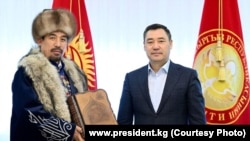 Манасчы Рысбай Исаков жана президент Садыр Жапаров.