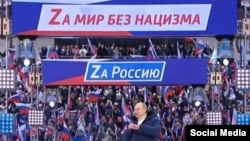 Vladimir Putin vorbind înaintea unui concert marcând anexarea Crimeii și Sevastopolului. Pe bannere se poate citi: Pentru Rusia. Moscova, 18 martie 2022