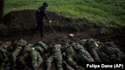Припадник на украински тим за деминирање проверува дали има експлозив околу телата на 11 руски војници во селото Вилхивка, кое беше вратено од украинските сили, во близина на Харкив на 9 мај.