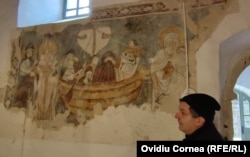 Parohul Zoltán Felházi, în fața unei picturi murale care înfățișează mai mulți pelerini în furtună, realizată în jurul anului 1.400.