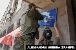 Російські військові змінюють табличку на міській раді окупованого українського Світлодарська. Травень 2022 року