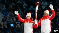 Динигеер Йиламуцзян (солдо) жана  Цзяфэн Чжао  (оңдо) Олимпиада отун көтөрүп бара жатышат. Бээжин, 4-февраль, 2022-жыл.