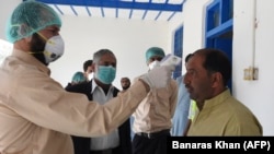 FILE: A doctor checks the temperature of a man returning from Iran at a quarantine zone to test for the COVID-19 coronavirus in the Pakistan-Iran border town of Taftan in February.