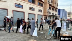 În imagine, palestinieni cară alimente lângă un depozit al filalei ONU pentru ajutorarea refugiaţilor din Fâşia Gaza, din Khan Younis sâmbătă 28 octombrie. Între timp, mii de oameni au dat năvală în mai multe depozite pentru a-şi procura minimul de alimente şi igienă.