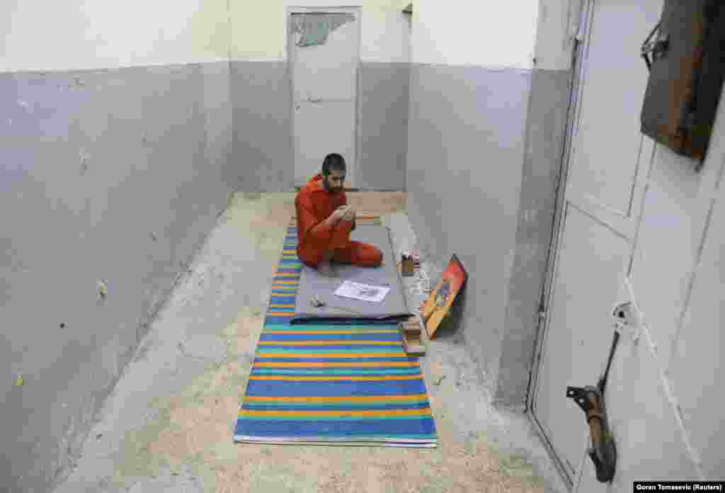 Abed El-Hamed Atiya, an Iraqi prisoner suspected of being part of the Islamic State group, sits next to a picture he drew inside a prison in Hasaka. He is kept apart from other prisoners, some of whom strongly object to his art.&nbsp;