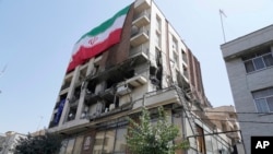 ირანის დროშა შენობაზე, რომელიც ივნისში ისრაელის საჰაერო დარტყმის შედეგად დაზარალდა.