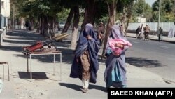 Două femei îmbrăcate în burca, trecând pe lângă armele talibanilor în Kabul. Poza a fost realizată în 1996, perioadă în care femeile trebuiau să se supună regulilor introduse de talibanii care conduceau țara.