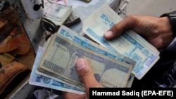 FILE: An Afghan currency exchange dealer waits for customers at a roadside in the southern Afghan city of Kandahar