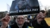 Архивна снимка от демонстрация в Брюксел през март 2025 г., която настоява ЕС да използва замразените руски активи в Европа, за да подкрепи Украйна. Жената на снимката носи плакат с надпис: „Накарайте Русия да си плати“.