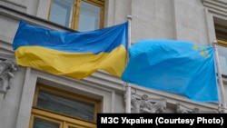 «Два флага – одна страна». Украинский государственный и крымскотатарский национальный флаги на флагштоках перед зданием МИД Украины в Киеве