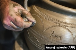 A potter twirls some ornamentation and the word "Zlakusa" into a raw pot before setting it to dry.