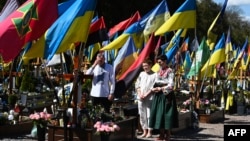 У велікодную нядзелю сям'я моліцца перад магілай загінулага ўкраінскага салдата на вайсковых могілках у Львове