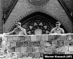 Двоє східнонімецьких робітників вкладають (вмуровують) бите скло на верхівку 15-метрової стіни, щоб запобігти спробам втечі берлінців із НДР до ФРН. Берлін, 22 серпня 1961 року