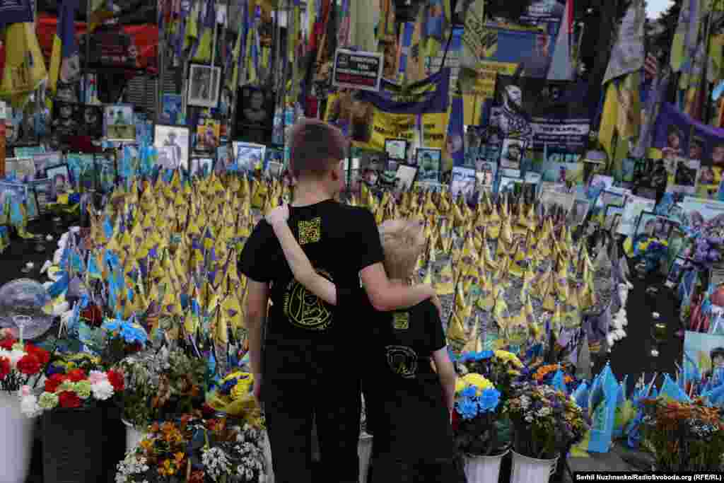 Дзеці, абняўшыся, глядзяць на народны сьцяжковы мэмарыял на мў айдане Незалежнасьці ў Кіеве. Ліпень 2025 году