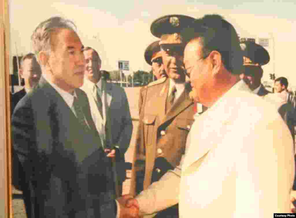 Заманбек Нуркадилов (справа) и первый президент Казахстана Нурсултан Назарбаев (слева). Фото, представленное в доме-музее Заманбека Нуркадилова.Нуркадилов, работавший акимом Алматы и Алматинской области, а затем занимавший пост председателя Агентства по чрезвычайным ситуациям, в марте 2004 года стал ярым критиком Нурсултана Назарбаева, тогда занимавшего пост президента, и его подчиненных. Что стало триггером конфликта, осталось неизвестным