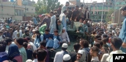 Taliban fighters and locals sit on an Afghan National Army vehicle on a street in Jalalabad Province on August 15..
