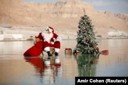 Баскетболчу Исса Кассиссие жомоктогу Санта-Клаустун кийимин кийип, Өлүк деңиздеги балатынын жанында сүрөткө түштү. Израилдик туризм министрлиги чет элдик туристтерди Ыйсанын туулган күнү жана Жаңы жыл майрамдарын белгилөө үчүн өз өлкөсүнө чакырып, ушул рекламалык сүрөттү даярдады. Эйн-Бокектин жаны. 2020-жылдын 15-ноябры.