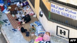 O familie strămutată care a fugit de violențele din sudul Libanului se adăpostește la intrarea unei sucursale a băncii iraniene Saderat din Sidon. 27 septembrie 2024.