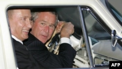 Президент США Джордж Буш (справа) схиляється над кермом, керуючи «Волгою» президента Росії Володимира Путіна 1956 року випуску перед вечерею двох лідерів 8 травня 2005 року в резиденції Путіна під Москвою