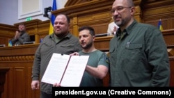 Volodimir Zelenski (centru), alături de prim-ministrul Denis Șmihal (dreapta) și președintele Radei, Ruslan Ștefanciuk, prezintă parlamentarilor declarația comună privind obținerea statutului de membru UE, 1 iulie