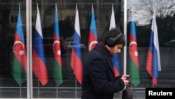 Озарбайжон ва Россия байроқлари олдидан ўтиб кетаётган шахс. Расм иллютрация учун ишлатилди. 