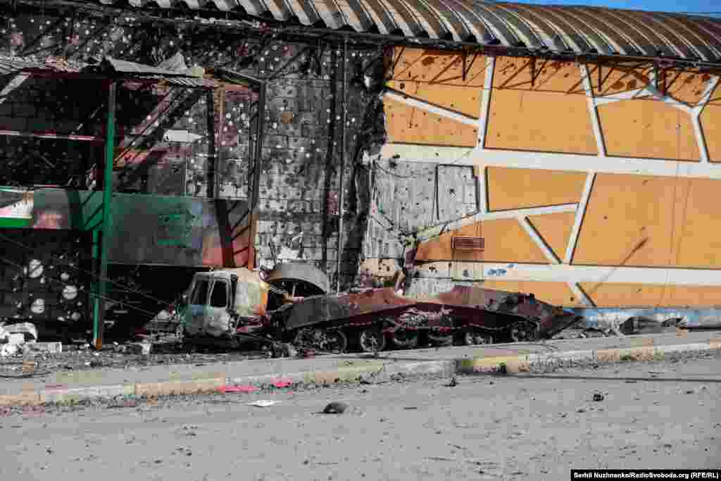 Зьнішчаная расейская тэхніка, побач разбураны гандлёвы цэнтар «Жыраф», дзе разьмяшчаліся пазыцыі ўкраінскіх вайскоўцаў.Гандлёвы цэнтар «Жыраф» быў адноўлены і адкрыты наноў.Зьлева фота 11 сакавіка 2022 году, справа — з сакавіка 2025 году