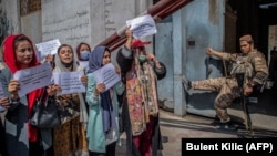 A Taliban fighter watches as Afghan women hold placards during a demonstration demanding better rights for women in front of the former Women's Affairs Ministry in Kabul on September 19.