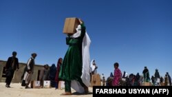 An internally displaced woman carries free aid distributed during the holy month of Ramadan in a refugee camp on the outskirts of Mazar-e Sharif.