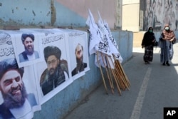 Femei afgane trecând pe lângă portrete ale liderilor talibani și steaguri în Kabul, Afganistan, august 2021.