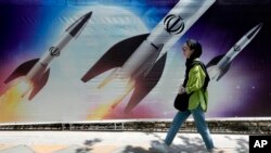 ირანელი ქალი ქუჩაში ბანერის ფონზე, რომელზეც გამოსახულია ირანული რაკეტების გაშვება. თეირანი. 2024 წლის აპრილი