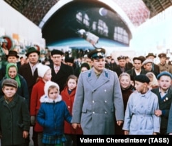 Юрий Гагарин жана кызы Елена (сол жакта атасы менен кол кармашып турат) СССРдин эл чарбасынын жетишкендиктери көргөзмөсүндө калайык менен. Москва. 1965-жылдын 19-октябры.