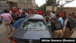 Police officers survey a damaged car at the site of an attack at the Pakistan Stock Exchange entrance in Karachi after a militant attack on June 29.