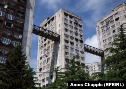 Blocuri de apartamente, într-o suburbie deluroasă din Tbilisi, cu punți amețitoare între ele, care permit oamenilor să se deplaseze rapid, fără eforturi extenuante. De exemplu, poți să urci cu liftul din blocul din stânga până la galerie, să treci prin pasarelă, prin blocul din mijloc, și să ajungi până la magazinul alimentar din blocul din dreapta, fără să trebuiască să mergi pe jos până în vârful dealului și apoi să cobori.
