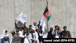 FILE: Afghan civilians carrying Afghan national flag along with Taliban fighters and Afghan army soldiers pose for a photograph during a brief cease-fire in 2018.