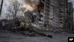 Украински полицай се прикрива пред горяща сграда, пострадала при руски въздушен удар в Авдиивка през март 2023 г