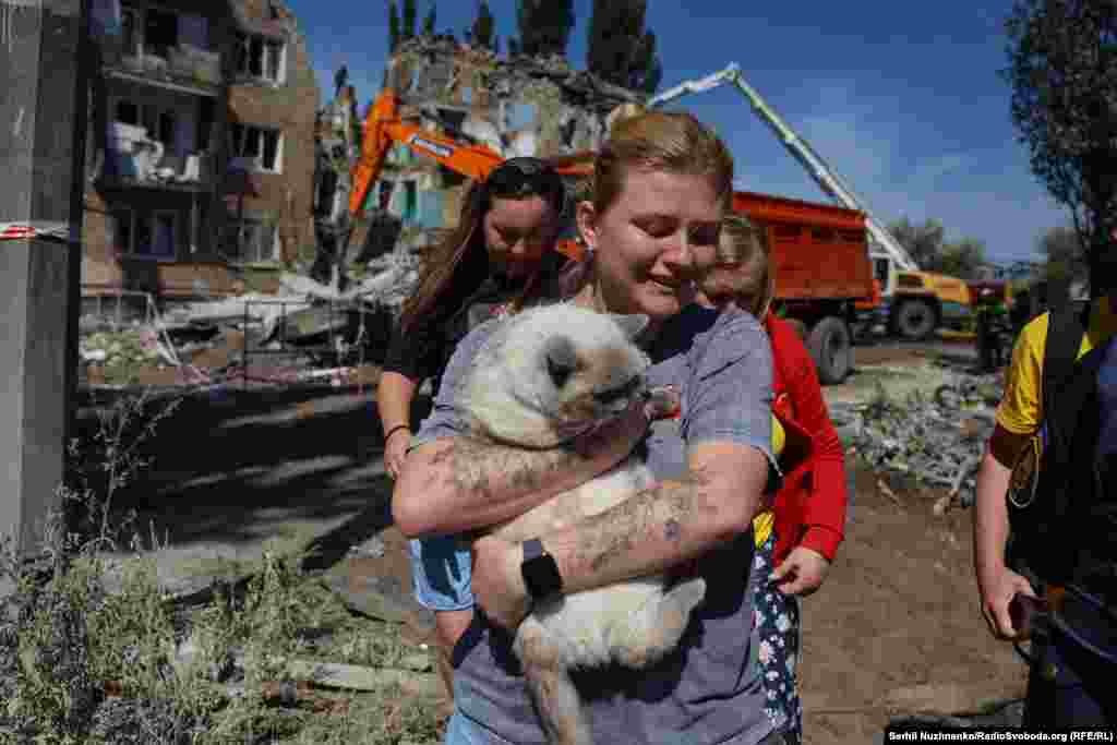 Aýal maşgala hüjüm edilen jaýyň harabalyklarynda halas edilen pişigi alyp barýar.